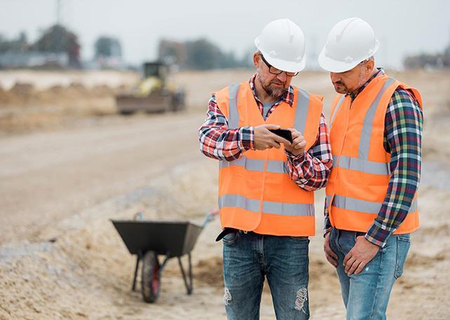 mężczyźni w kamizelkach odblaskowych i hełmach patrząca w telefon